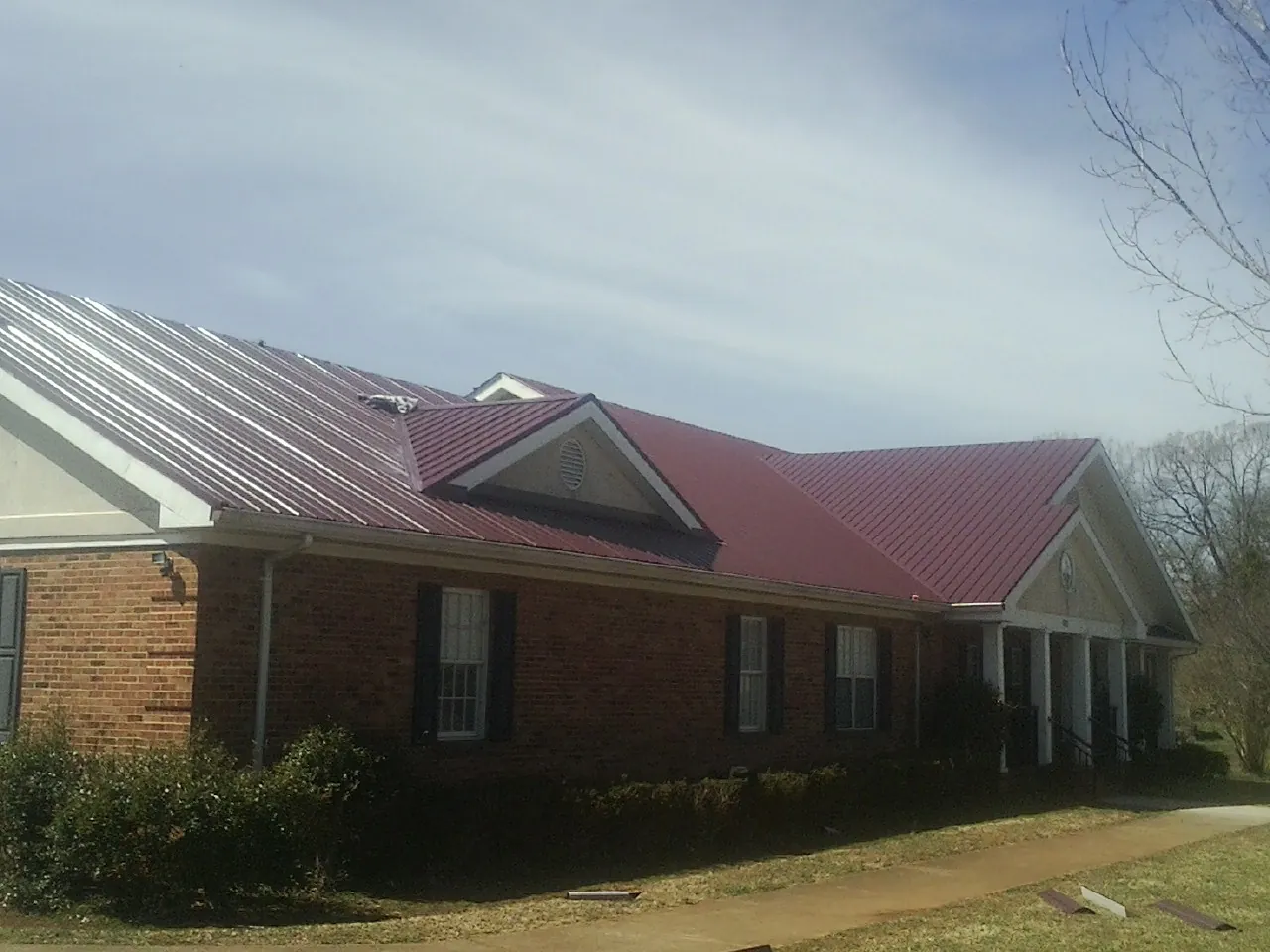 Red metal roof with gabled entries on a long brick building, from a Hail Damage Roof Repair job in Mc Connellsburg