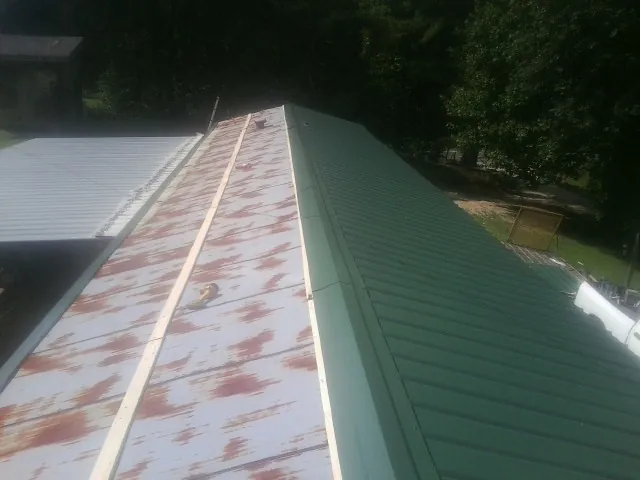 Old rusted panels beside newly installed green metal roofing — Wind Damage Roof Repair by Roofing Brothers in Mc Connellsburg