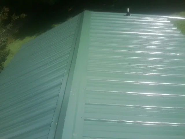 New green metal panels meeting at the ridge of a roof — Flat Roof Repair work by our crew in Mc Connellsburg