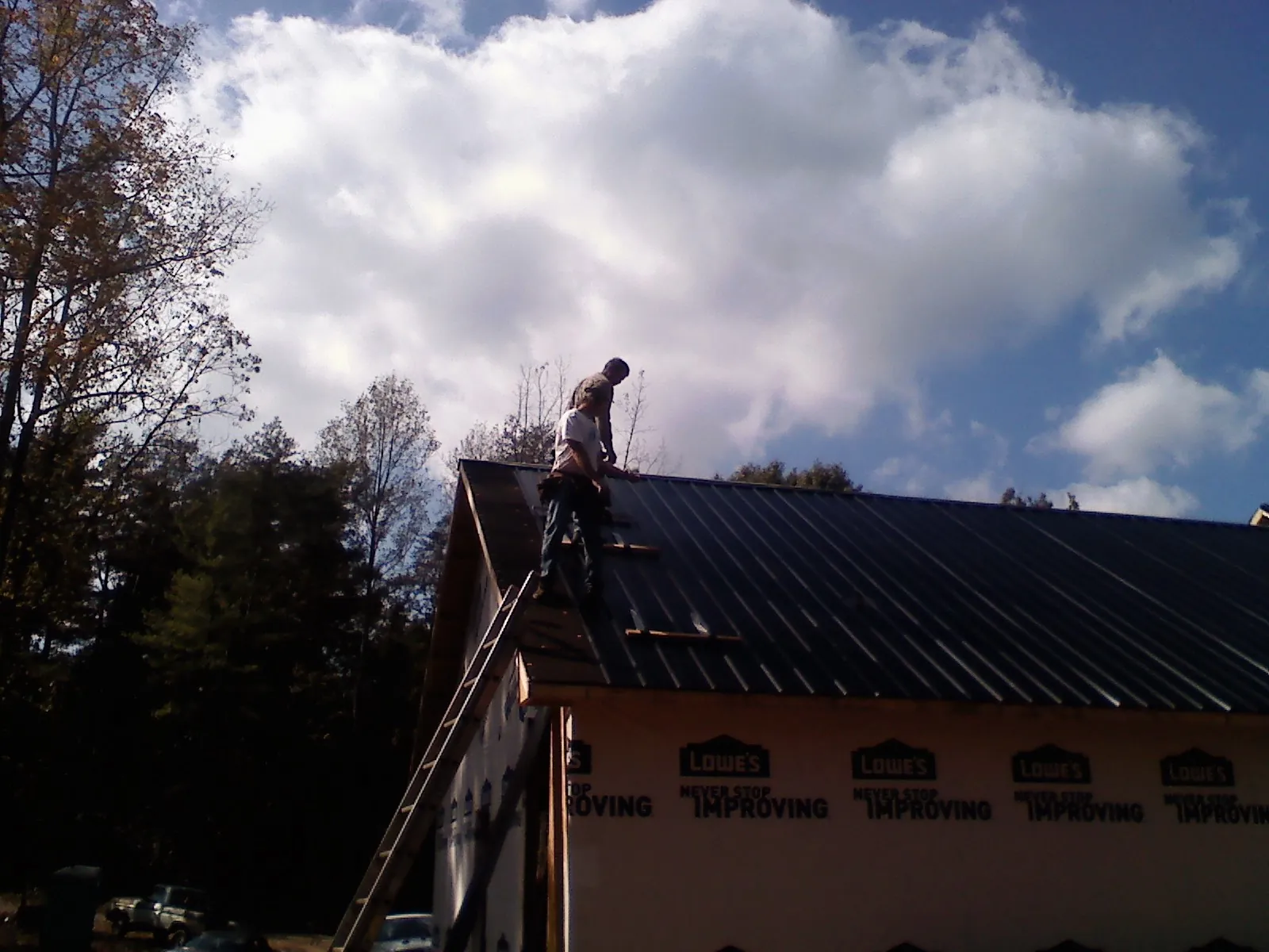 Roofer fastening dark metal panels high against a cloudy sky, from a Roof Inspection job in Mc Connellsburg