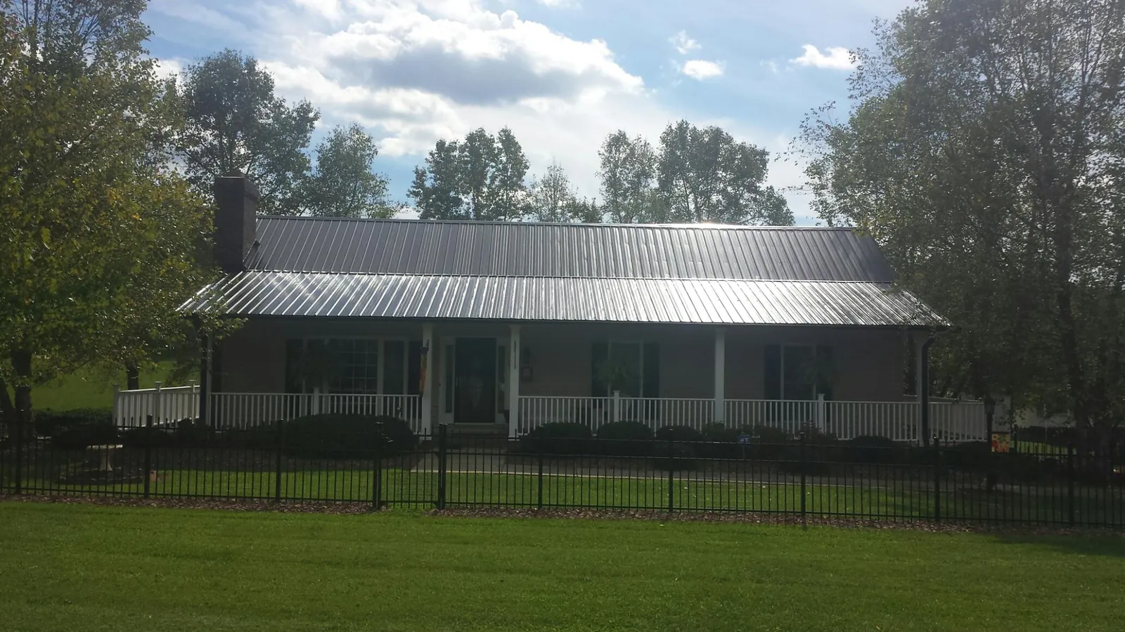 Gray metal roof on a brick ranch with a full width front porch — Gutter Guard Installation work by our crew in Mc Connellsburg