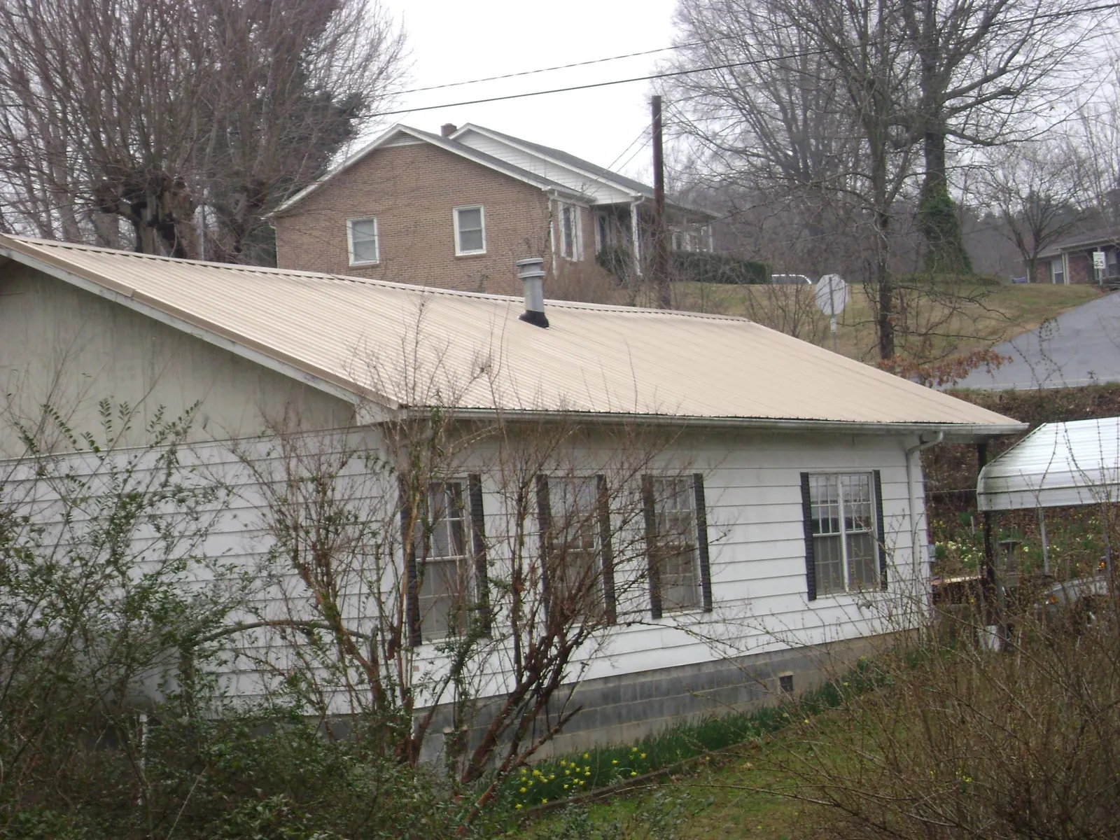 Tan metal roof on a white sided house set into a hillside — Commercial Roofing by Roofing Brothers in Mc Connellsburg
